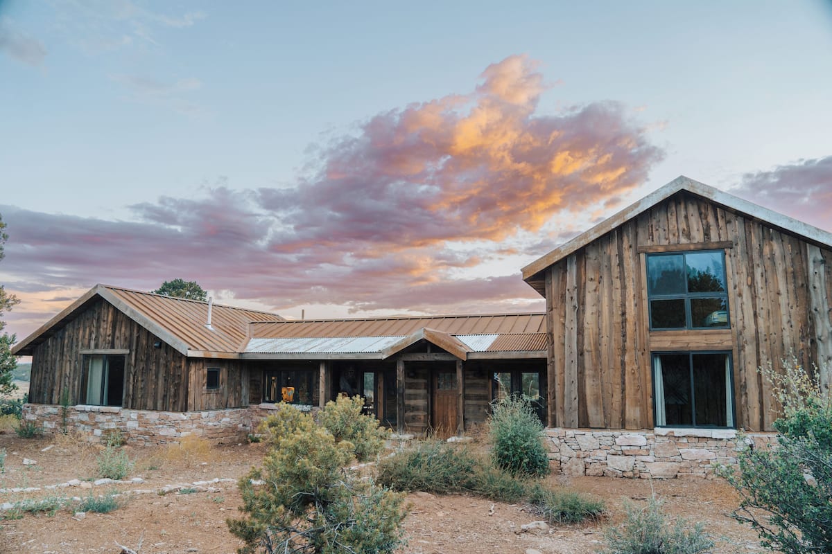A rustic wooden building with a stone foundation, large windows, and a metal roof.