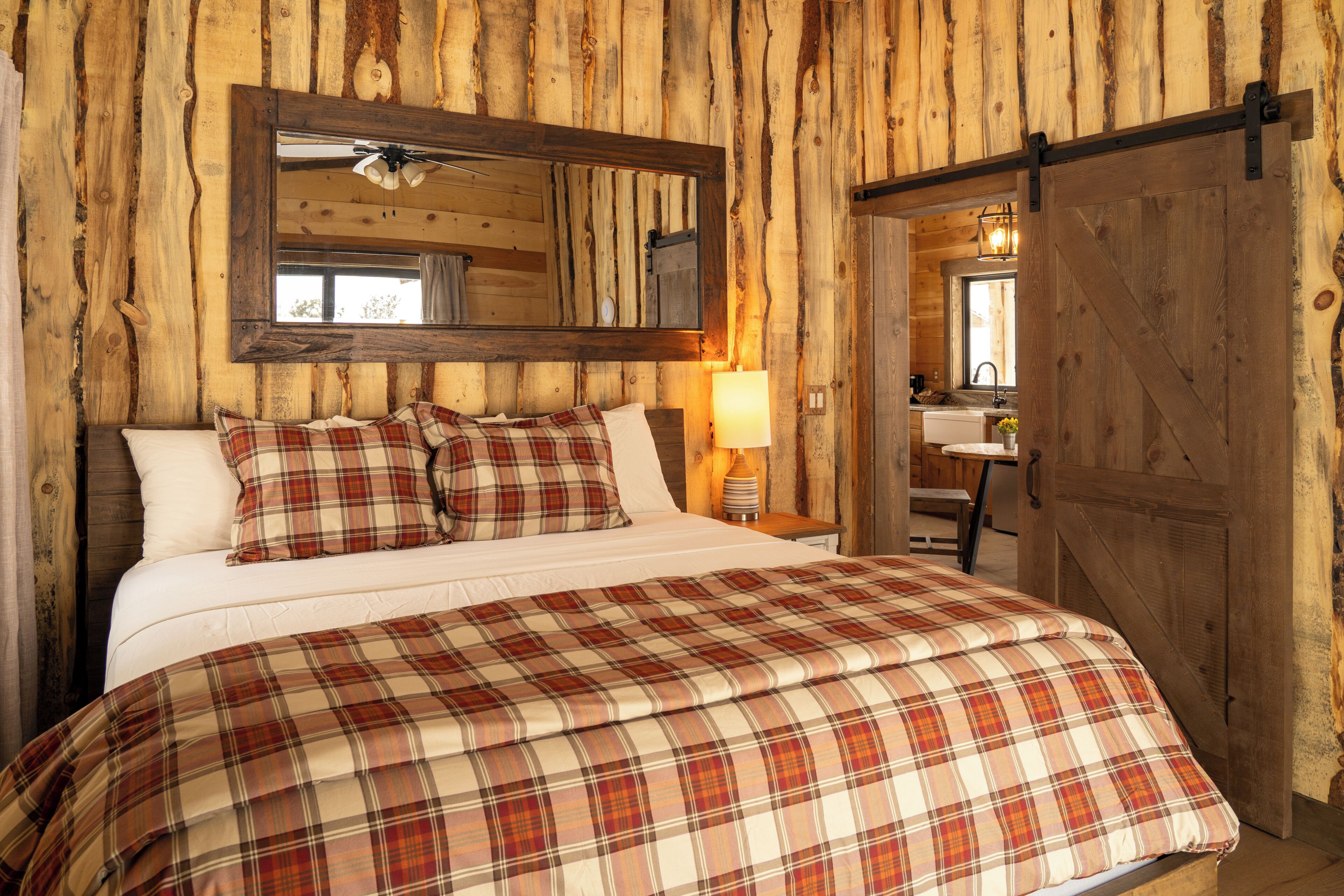 A wooden cabin-style bedroom with a large bed, a ceiling fan, a mirror, and a wooden door.