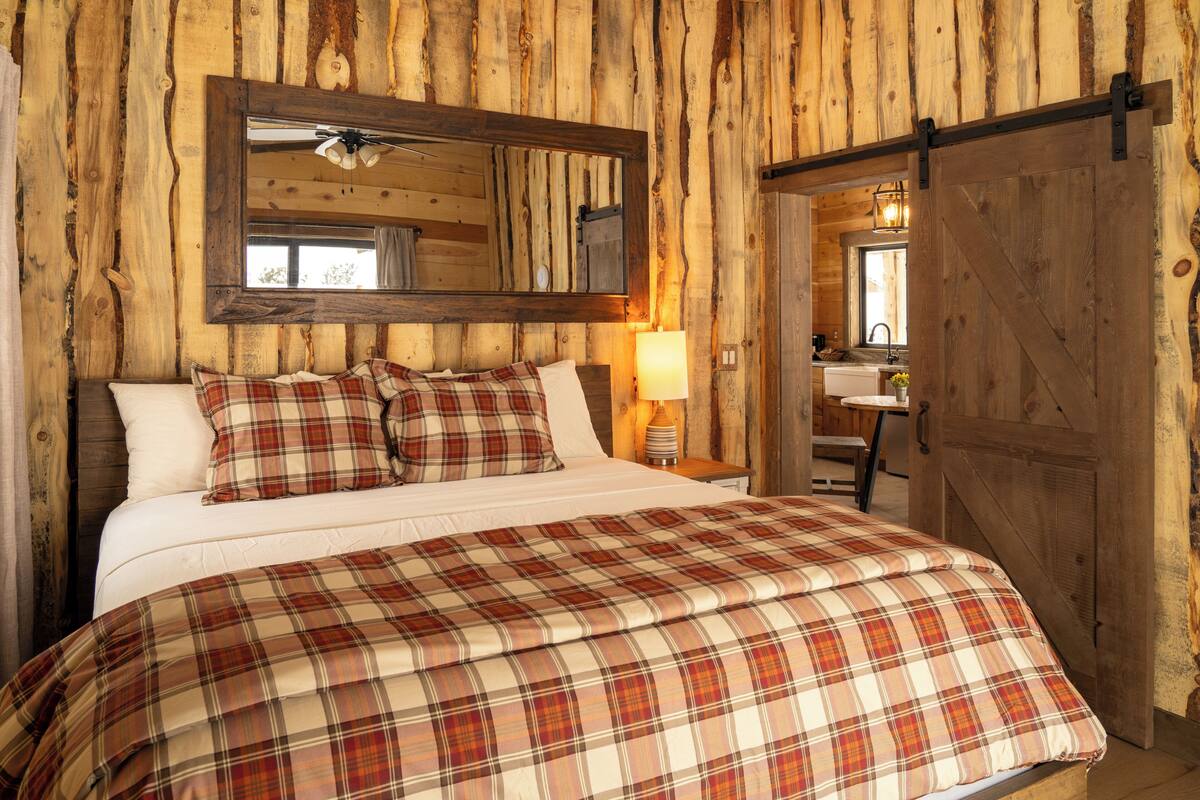 A wooden cabin-style bedroom with a large bed, a ceiling fan, a mirror, and a wooden door.