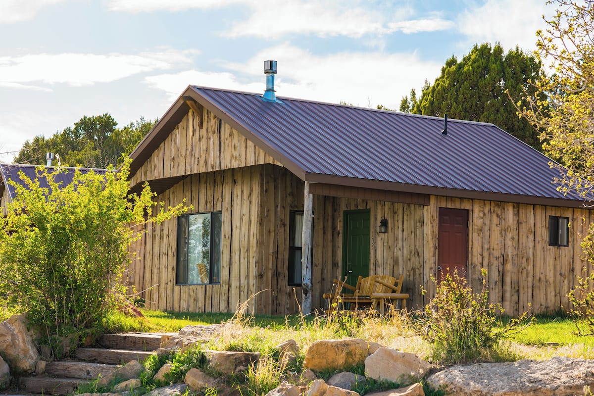A rustic wooden cabin with a sloped metal roof, a green door, and a bench outside.