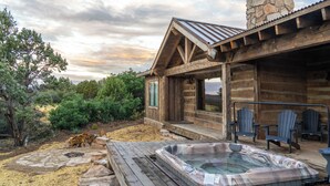 Una cabaña de madera con jacuzzi, sillas Adirondack y una chimenea de piedra.