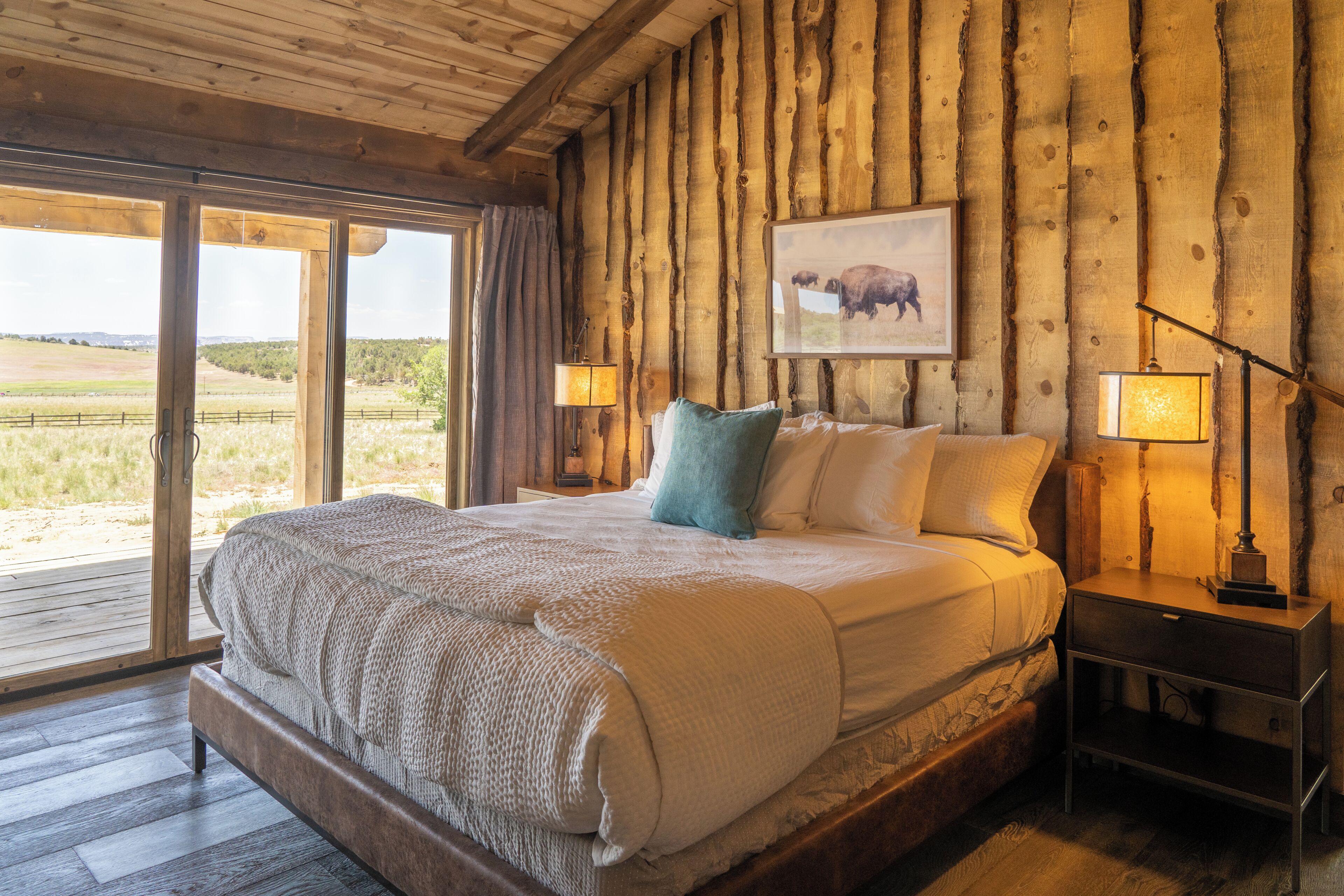 A wooden-framed room with a large bed, two bedside lamps, and a window with a view of the outdoors.