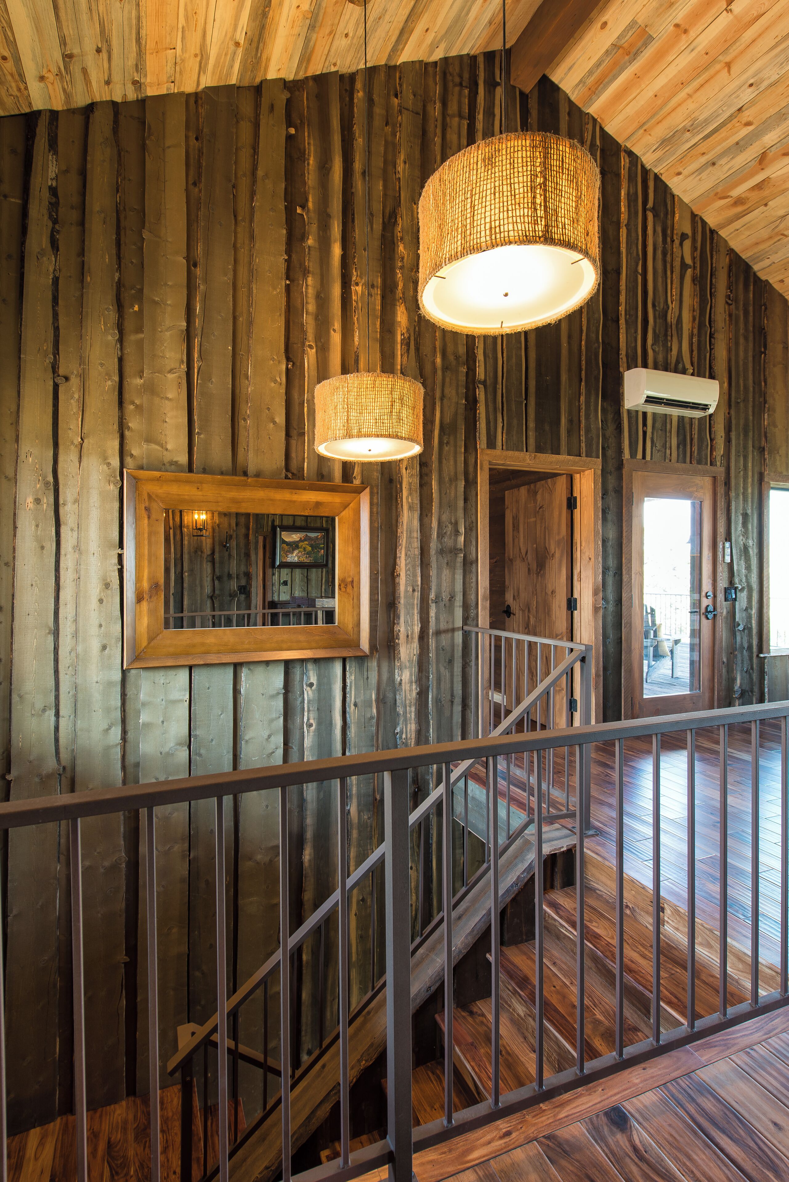 A wooden interior with a staircase, a hanging light fixture, and a framed picture on the wall.