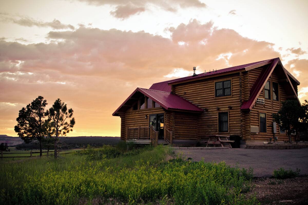 A log cabin with a red roof, a porch, and a picnic table.