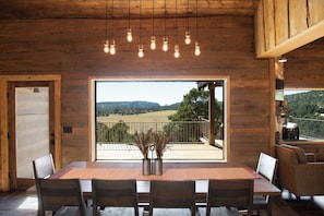 A wooden interior with a dining table, chairs, a view through a large window, and hanging light fixtures. - Zion Mountain Ranch (Mount Carmel)