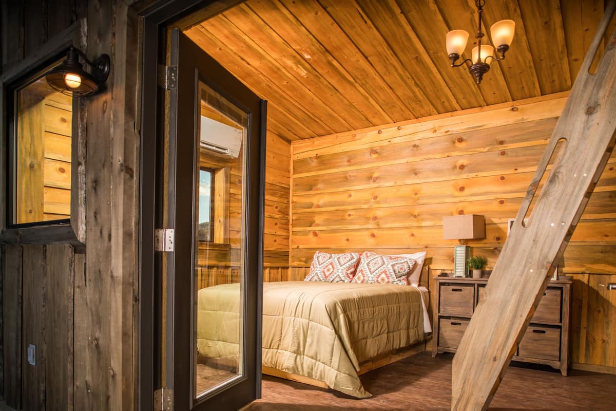 A wooden cabin bedroom with a bed, bedside tables, and a hanging light fixture.