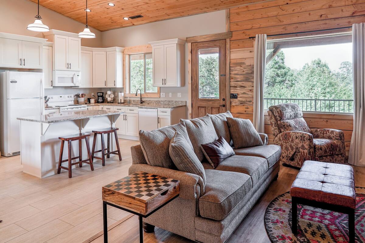 A modern kitchen with white cabinets, a central island with stools, a sofa, and a chessboard.