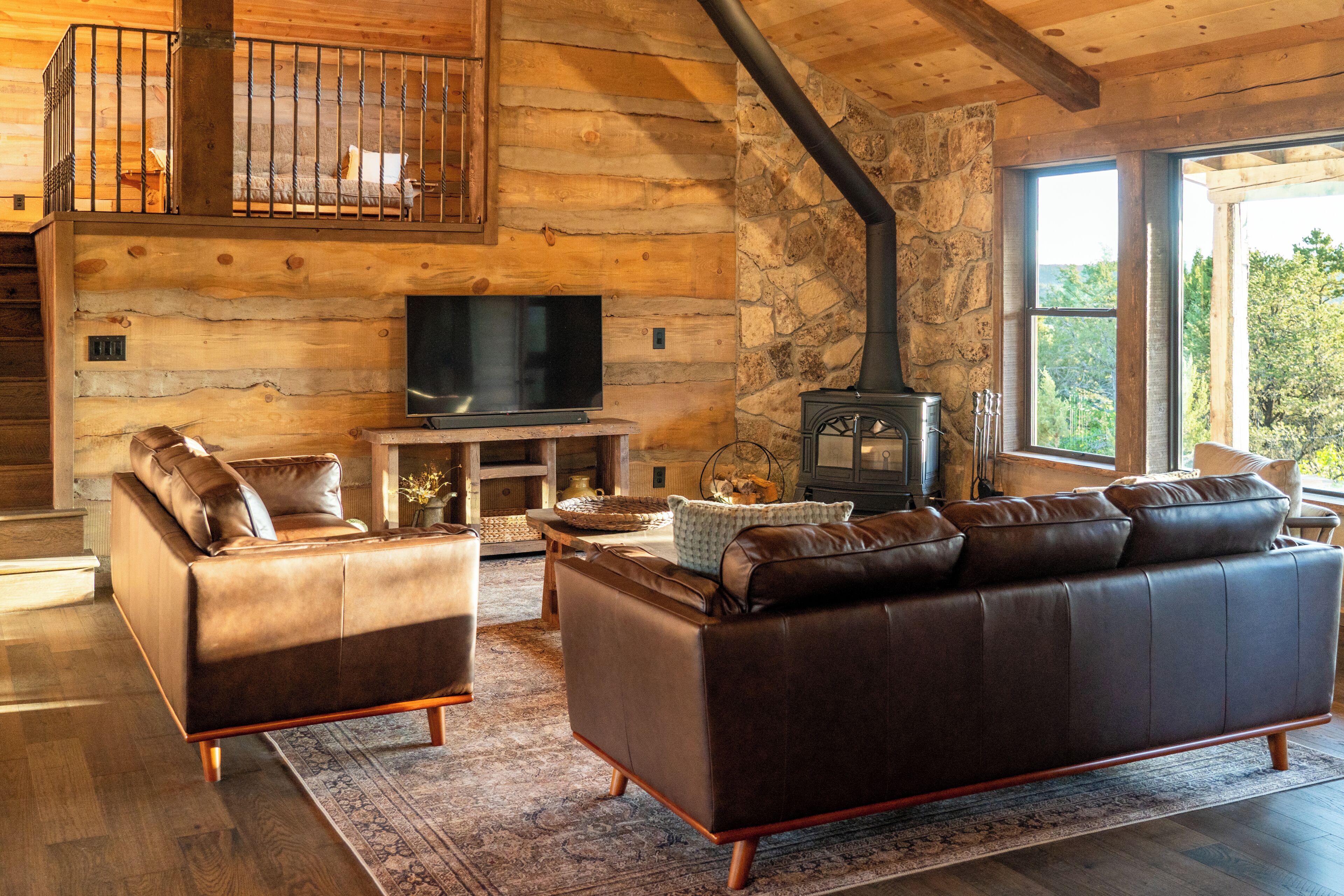 A log cabin interior with a fireplace, leather sofas, a television, and a stone wall.