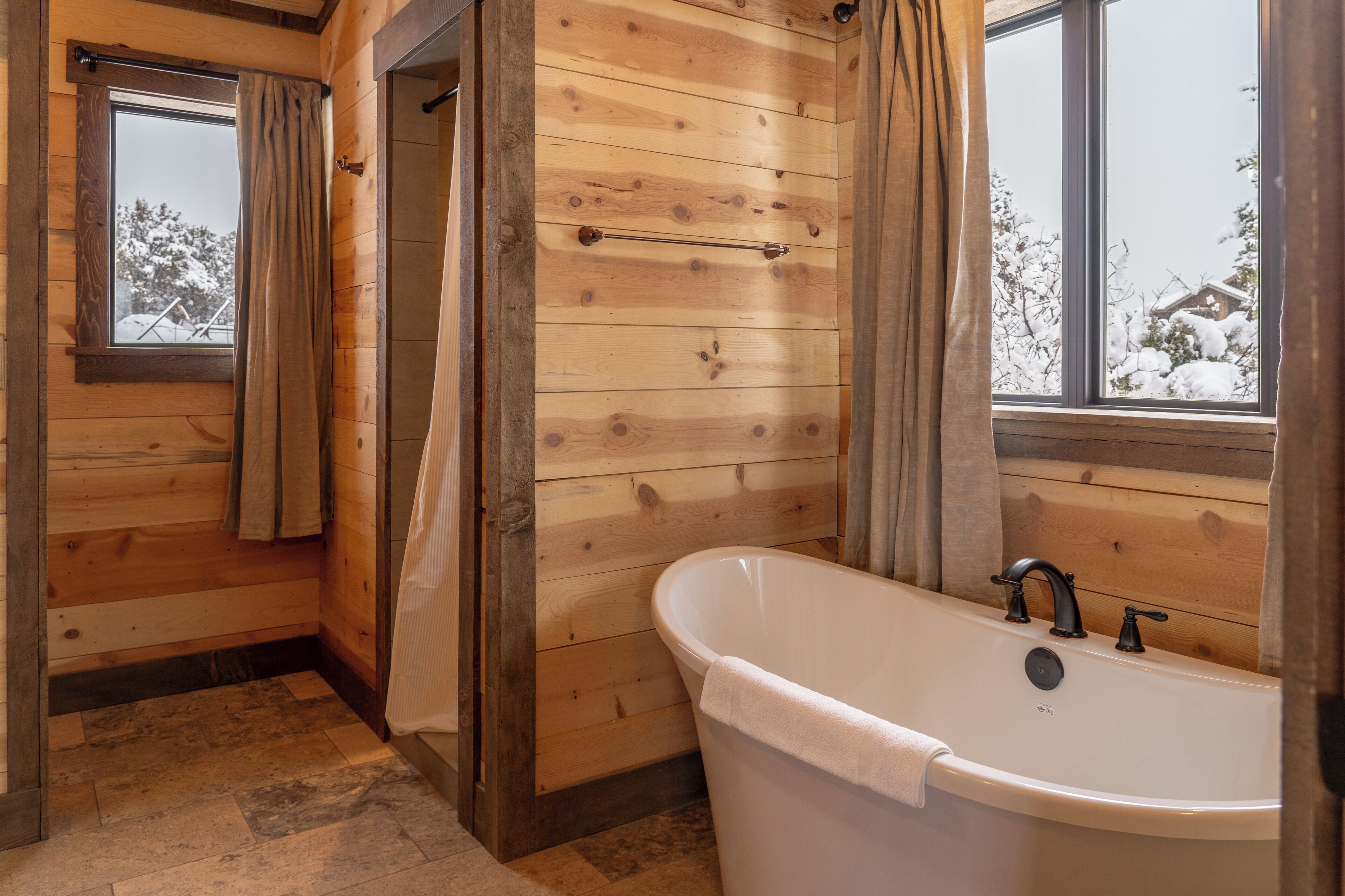Un baño con paneles de madera, una bañera, un perchero para toallas y un ventanal con cortinas.