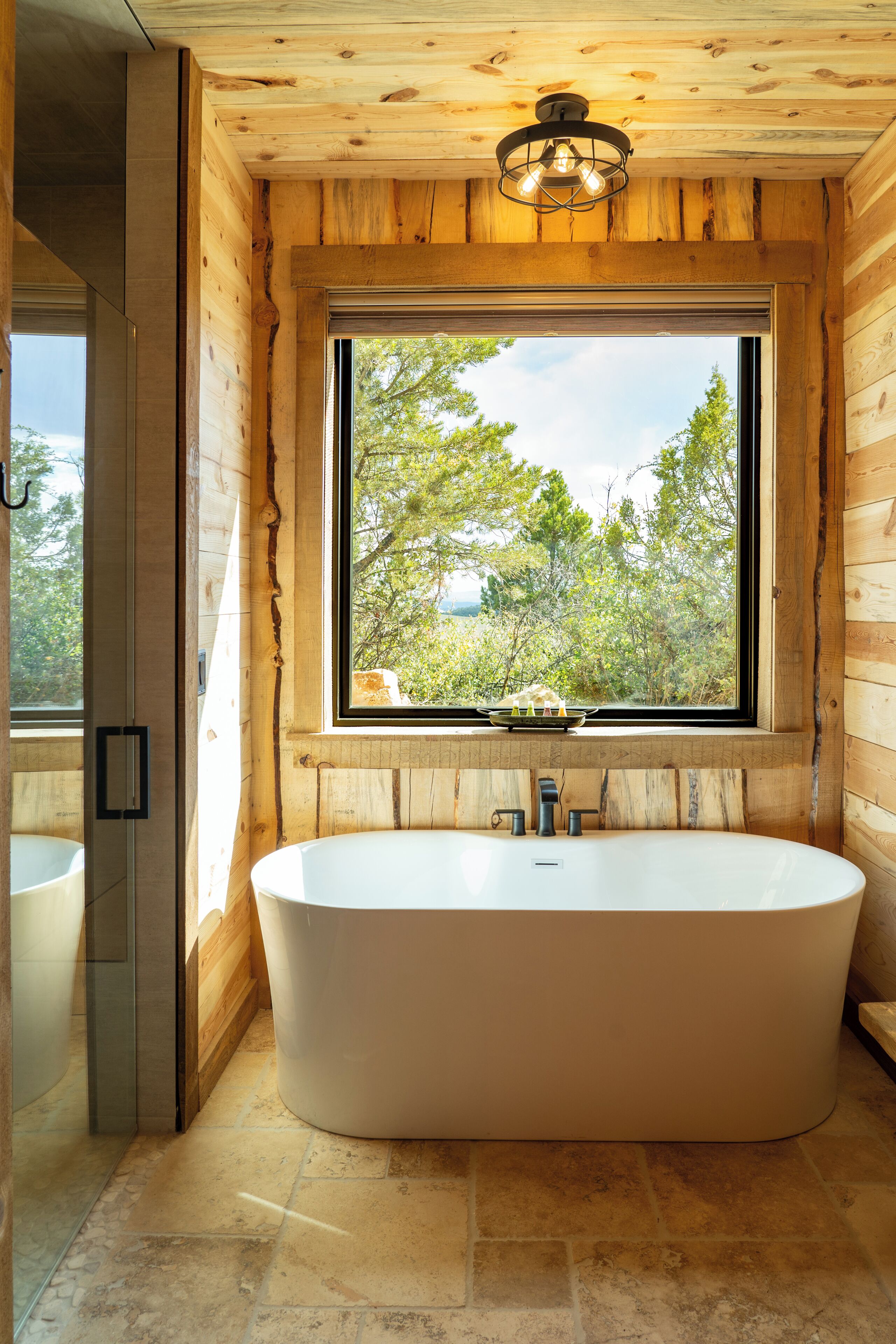 Une salle de bain moderne avec une baignoire sur pieds, une fenêtre donnant sur la forêt et des murs en bois.