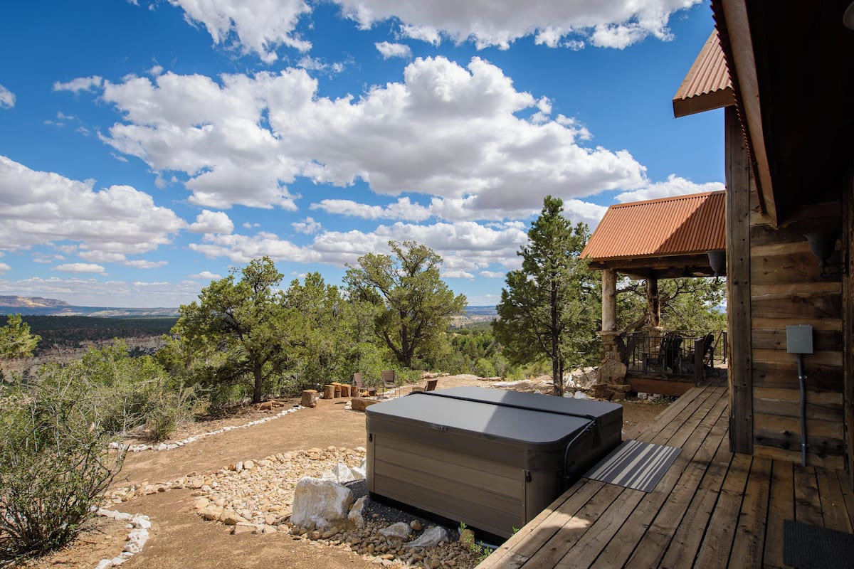A wooden cabin with a hot tub, outdoor seating, and a view of the mountains.