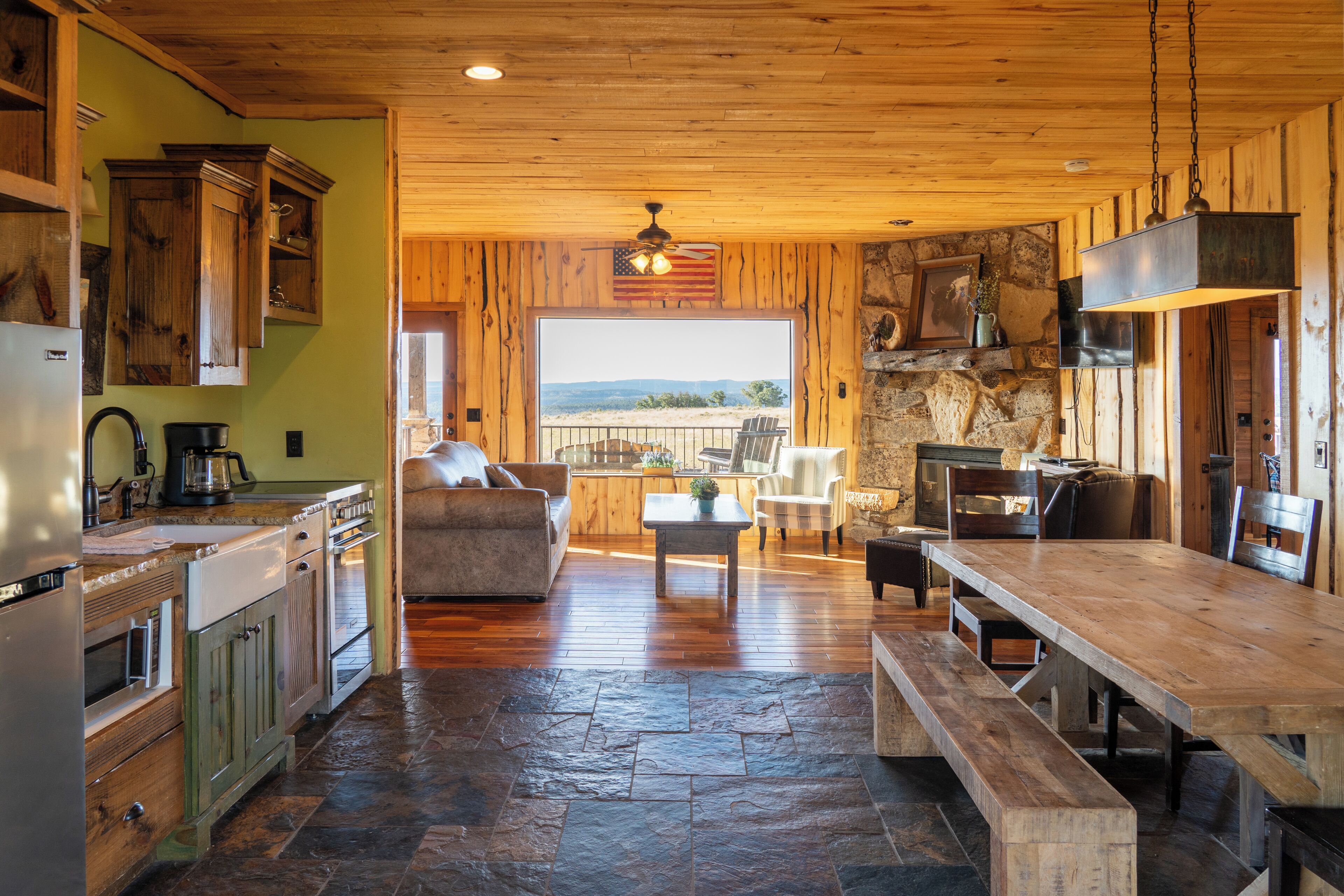 A rustic kitchen with wooden cabinets, a stone floor, and a large dining table.