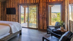 Una habitación de madera con una cama, un sofá y una mesa con una planta. Hay puertas correderas grandes que dan a un espacio exterior.