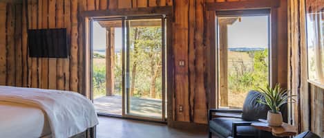 Une pièce en bois avec un lit, un canapé et une table sur laquelle est posée une plante. De grandes portes coulissantes donnent sur un espace extérieur.