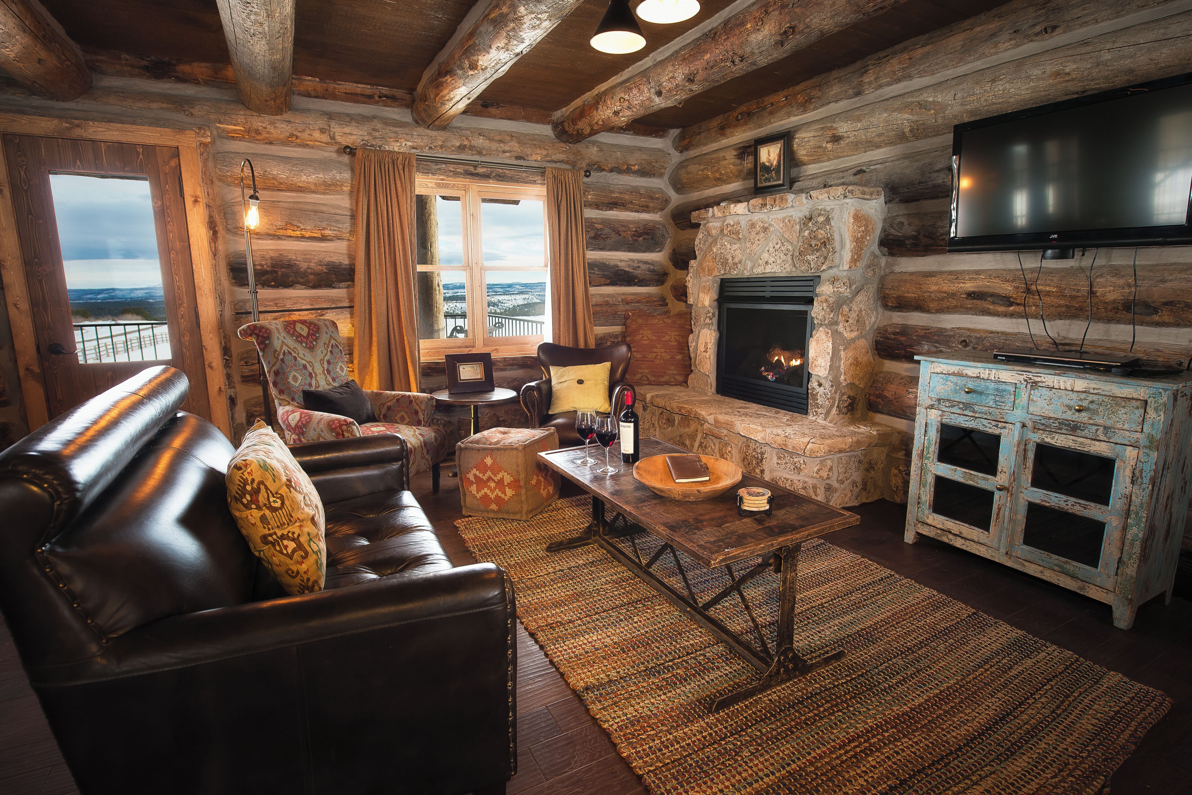 Ein Holzblockhaus-Interieur mit Kamin, Ledersofa und an der Wand befestigtem Fernseher.