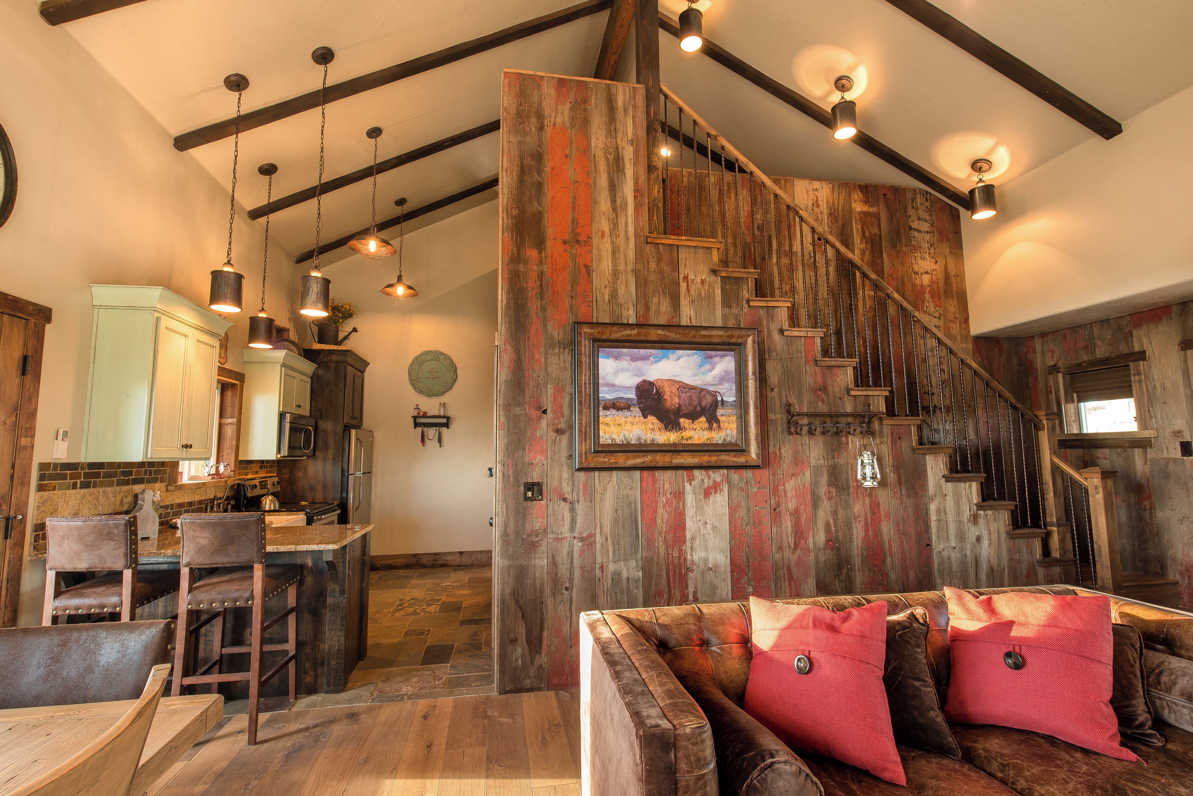 Un interior rústico con una escalera de madera, una zona de bar y un área de descanso con un cuadro grande.