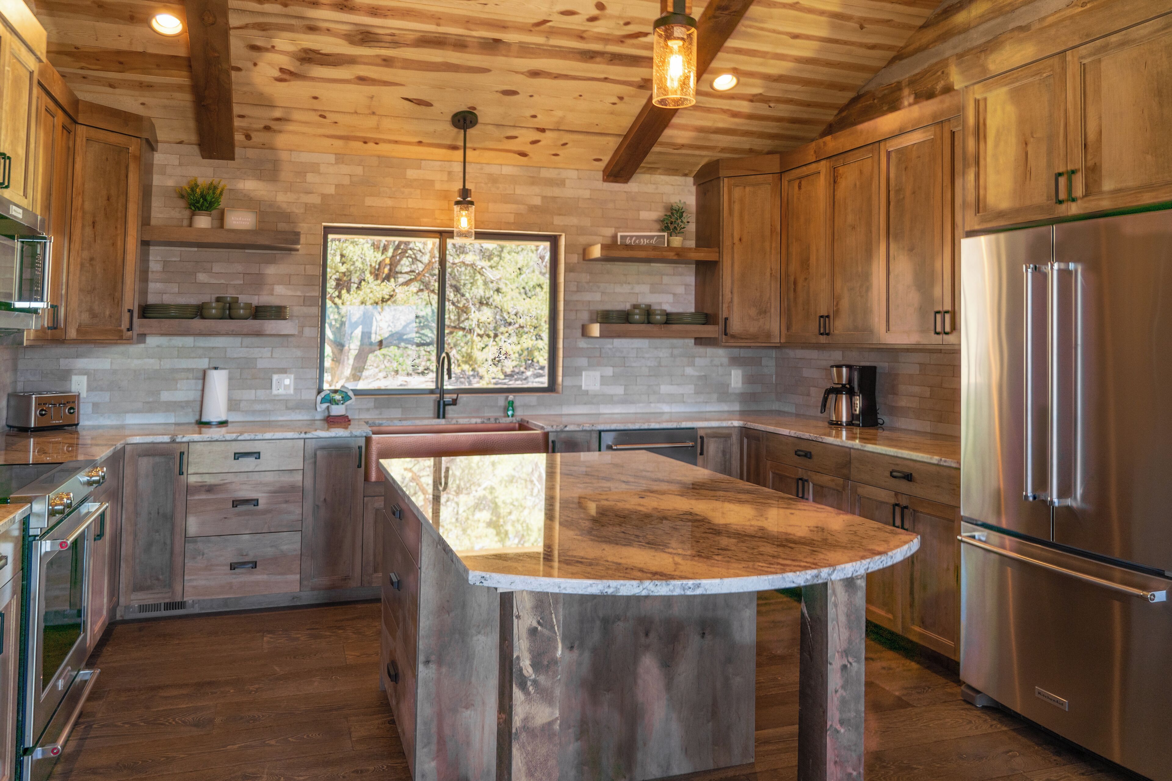 A kitchen with wooden cabinets, a large island, stainless steel appliances, and a window with a view.