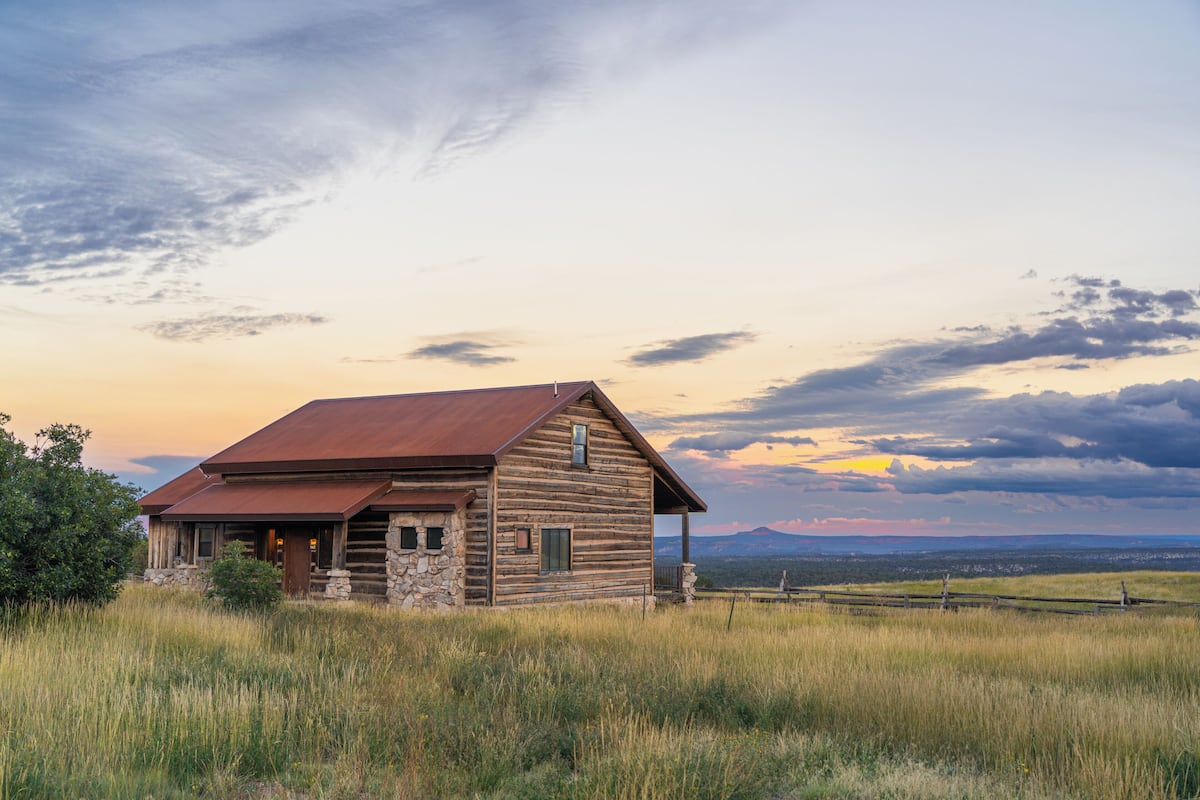 A rustic log cabin with a stone foundation, a metal roof, and a front porch.