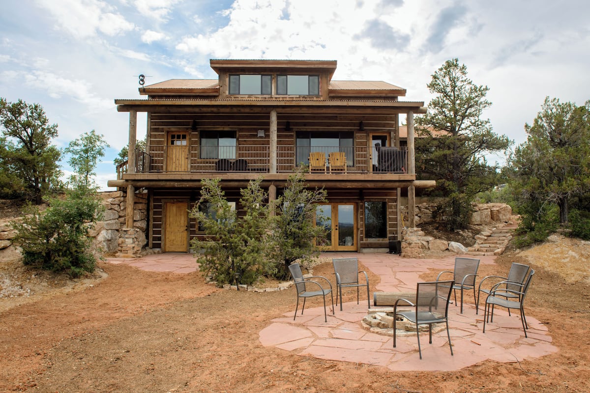 A two-story log cabin with a balcony, stone steps, and outdoor seating.