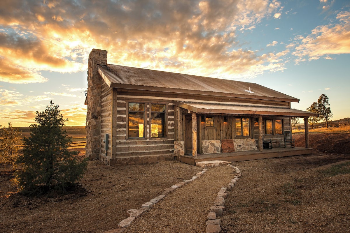 A rustic log cabin with a porch, large windows, and a stone chimney.