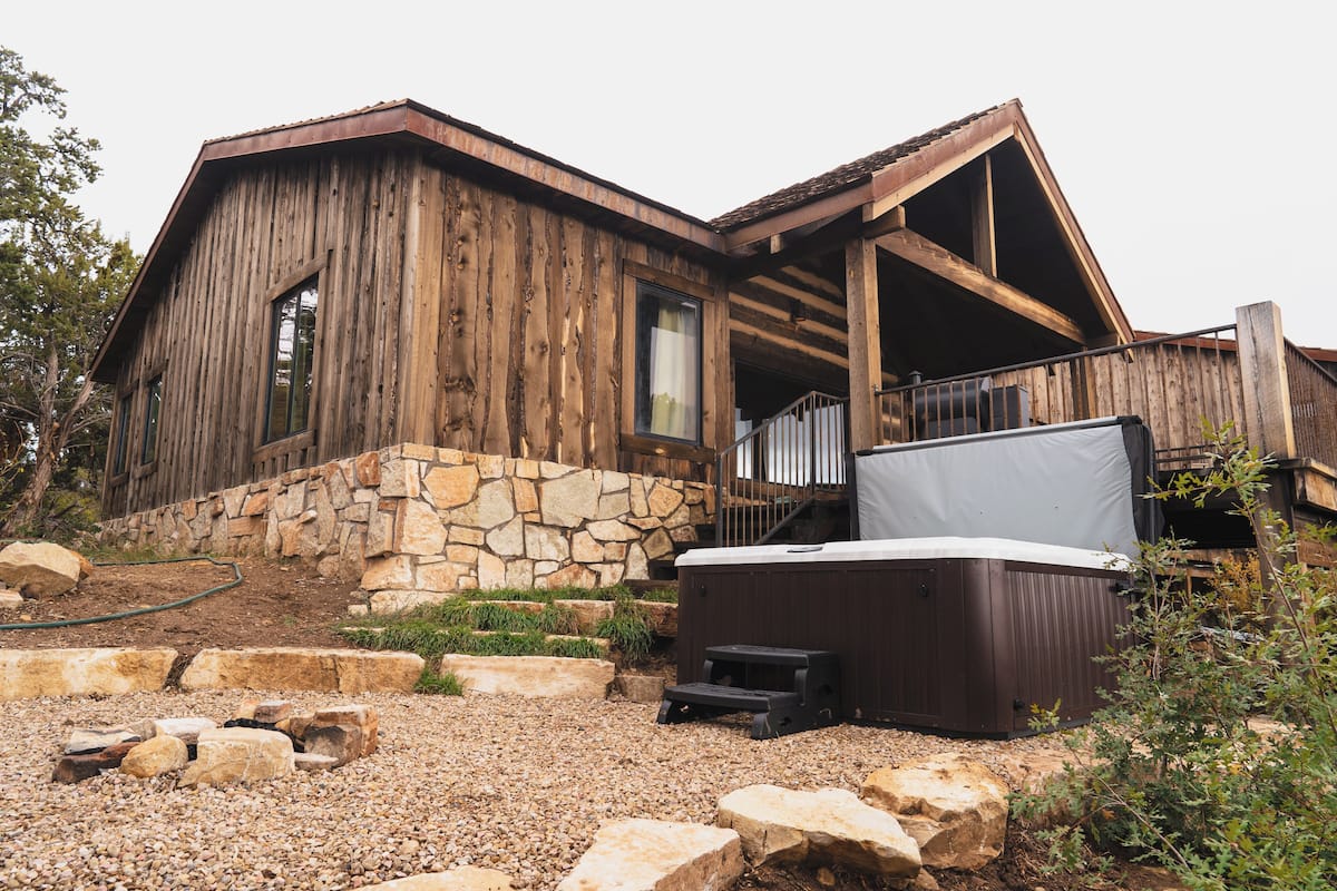 A rustic wooden cabin with a stone foundation, a hot tub, and a stone staircase leading to a porch.
