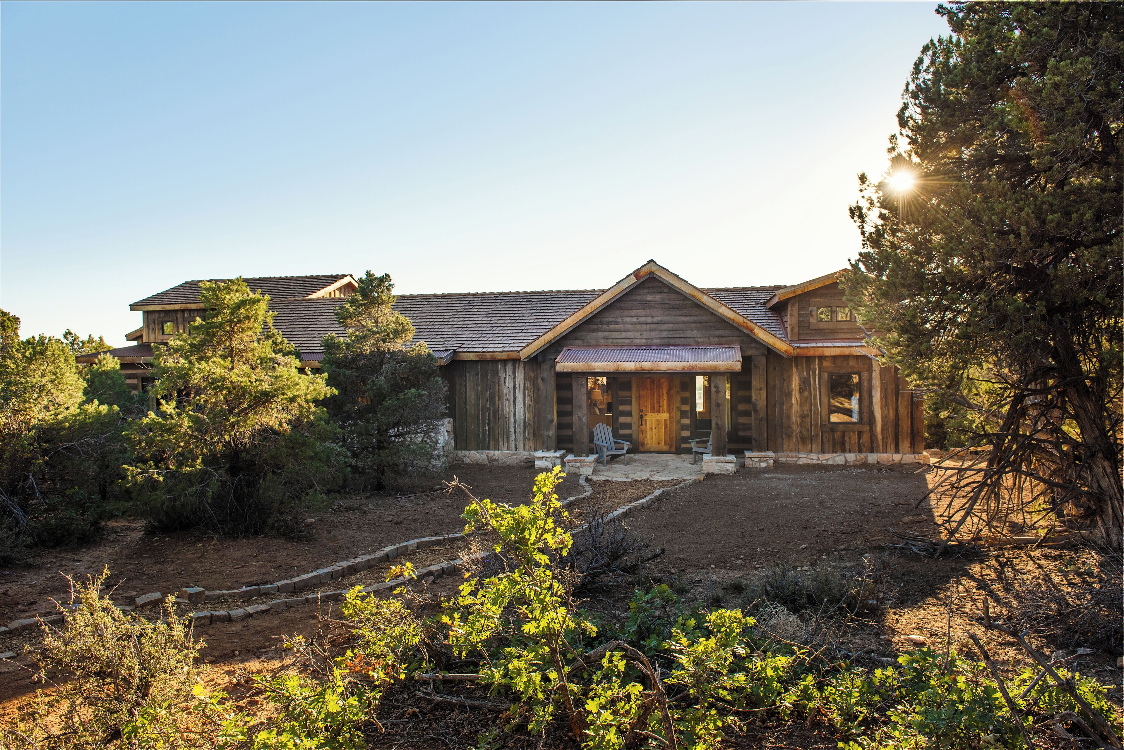 A wooden cabin with a front porch, surrounded by trees and a dirt path.
