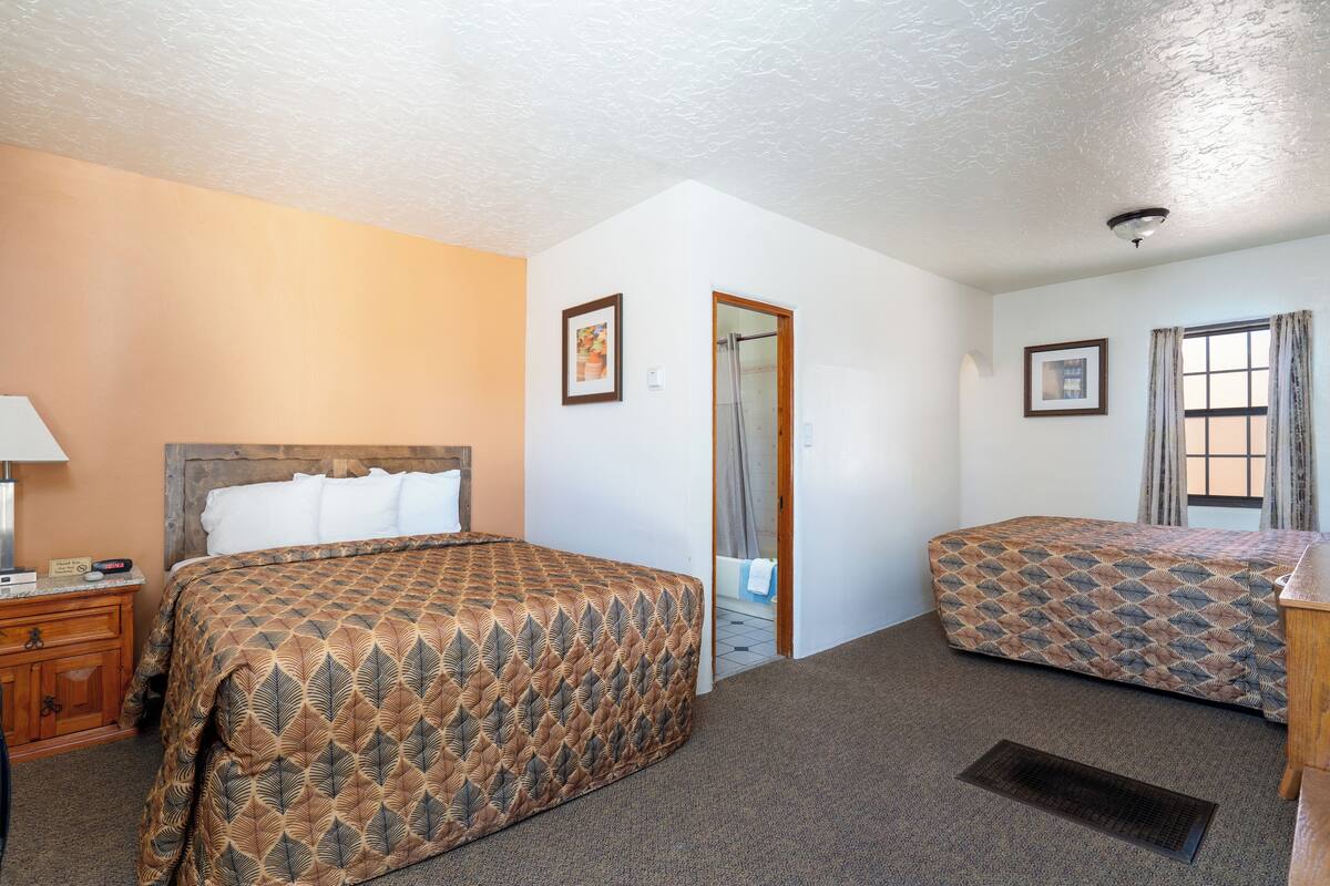 A hotel room with two beds, a wooden headboard, a nightstand, and a bathroom door.