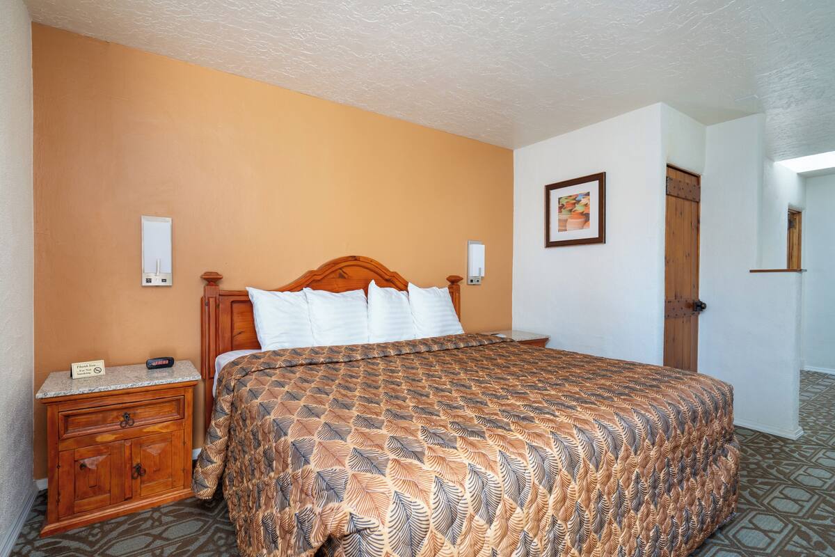 A hotel room with a large bed, wooden headboard, two bedside tables, a nightstand, and a door leading to another room.