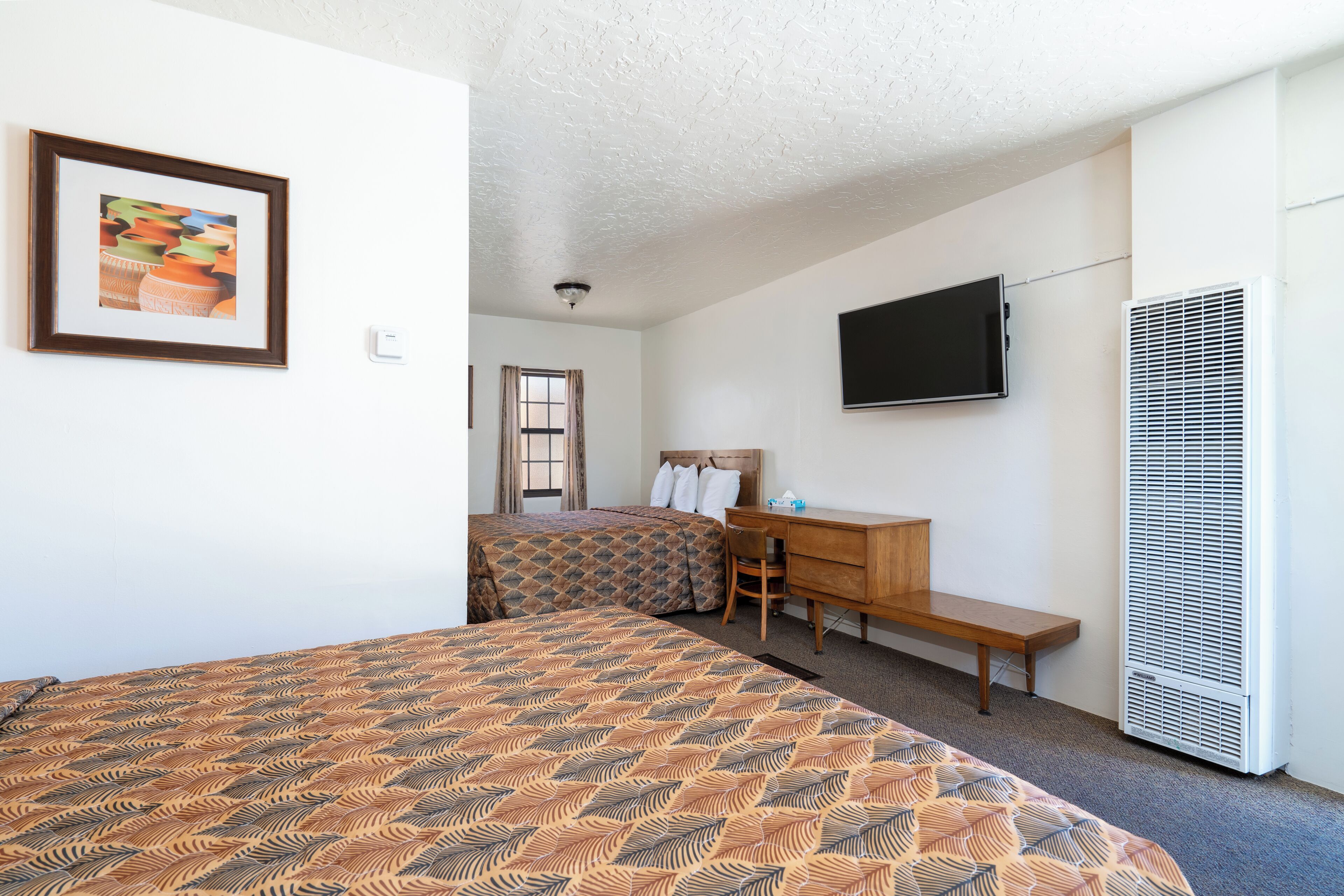 Habitación de hotel con dos camas, un escritorio, una silla, un televisor y un calentador.