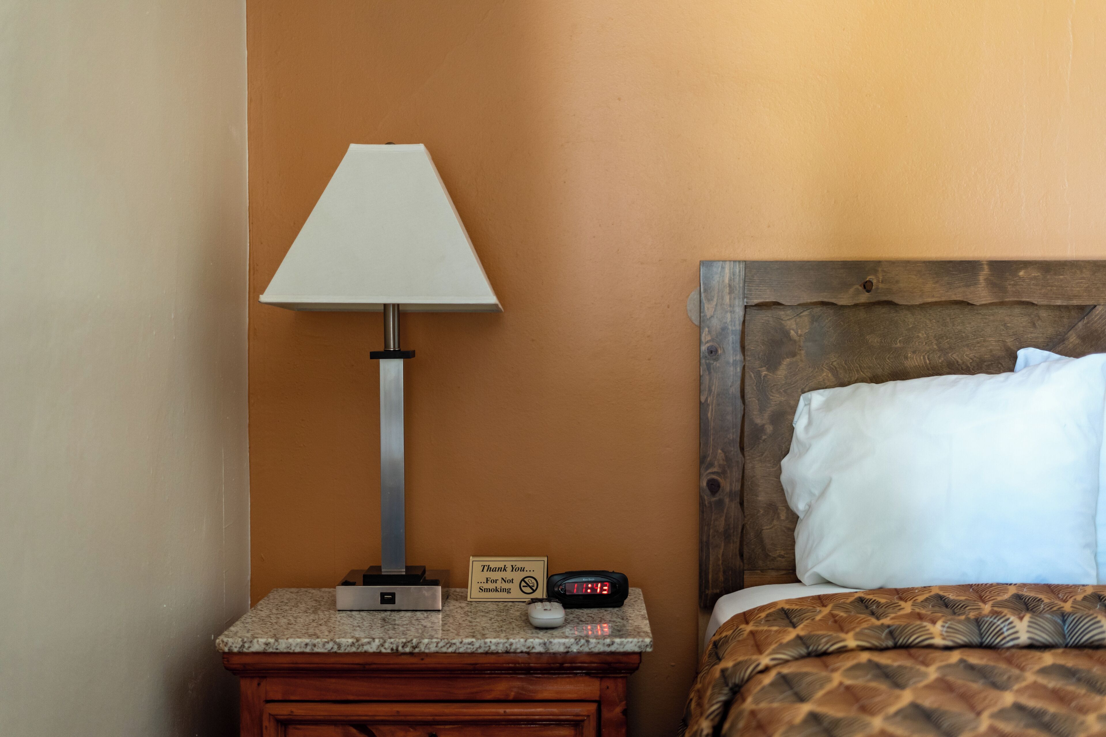 Una cama bien tendida con una colcha estampada, una almohada blanca y un cabecero de madera.