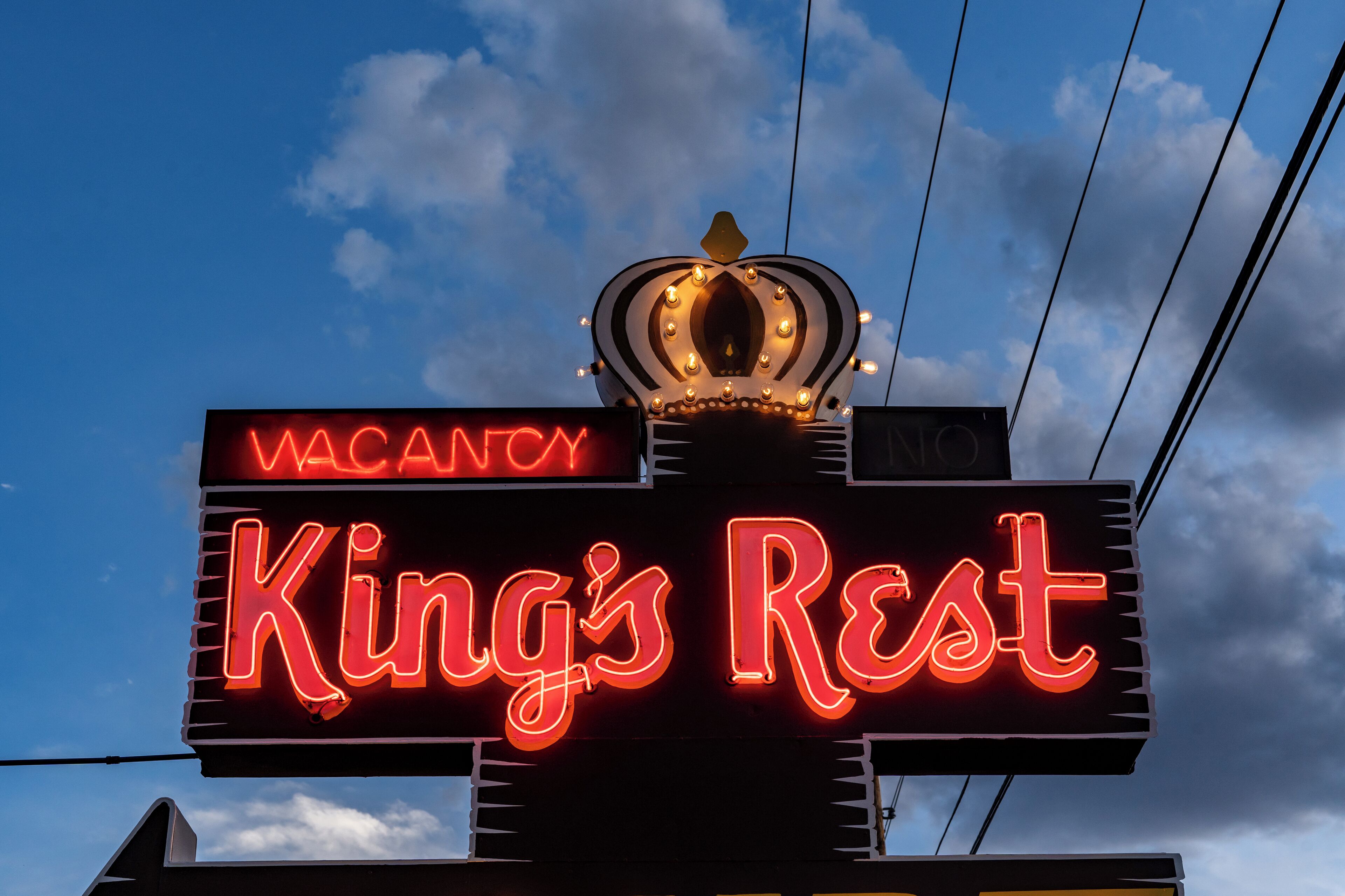 Letrero de neón que dice 'King's Rest' con un símbolo de corona en la parte superior, indicando disponibilidad.