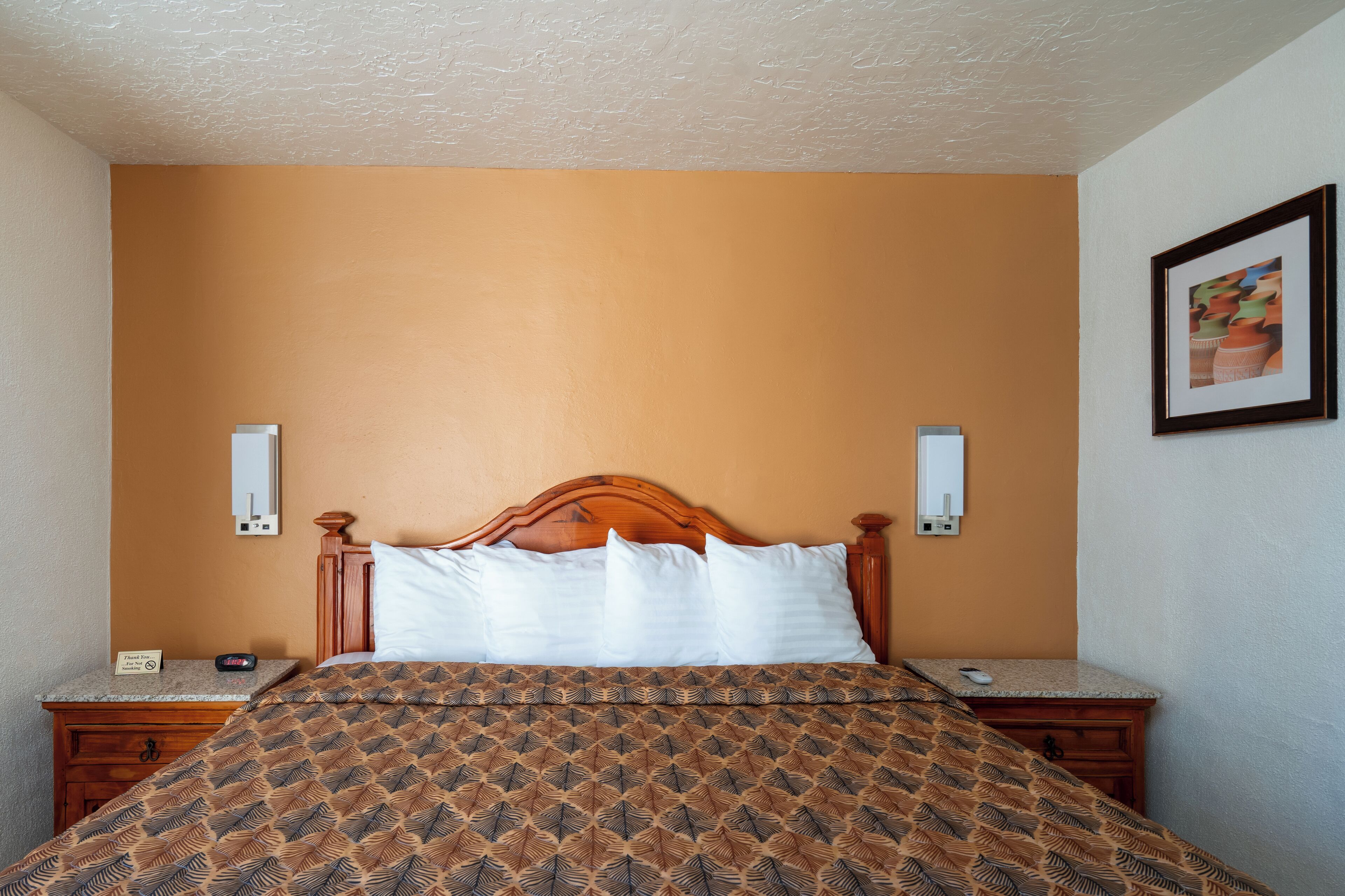 A hotel room with a wooden bed, a nightstand with a phone, and a framed picture on the wall.