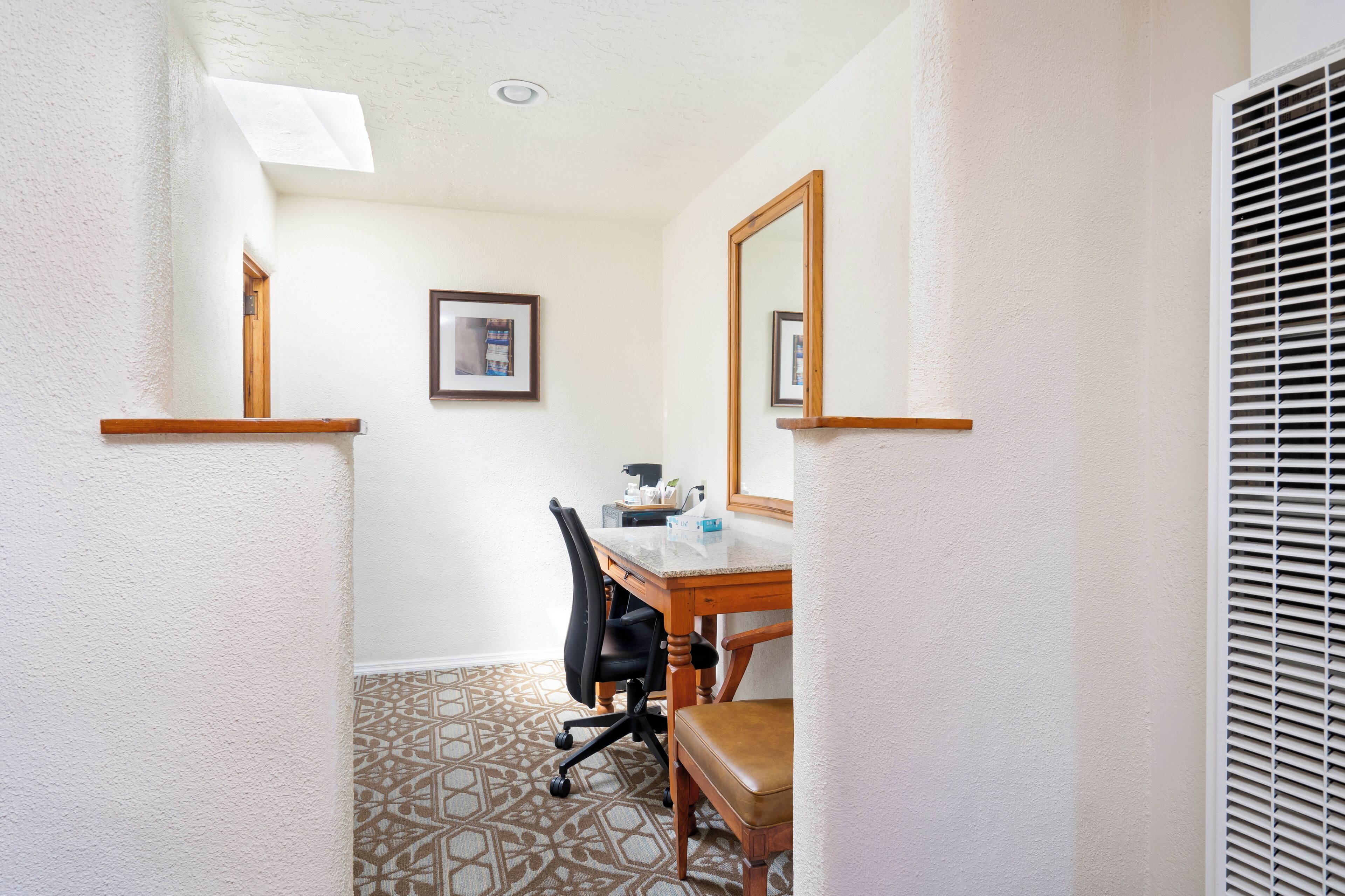 A hotel room with a wooden desk, a chair, a mirror, and a patterned floor.