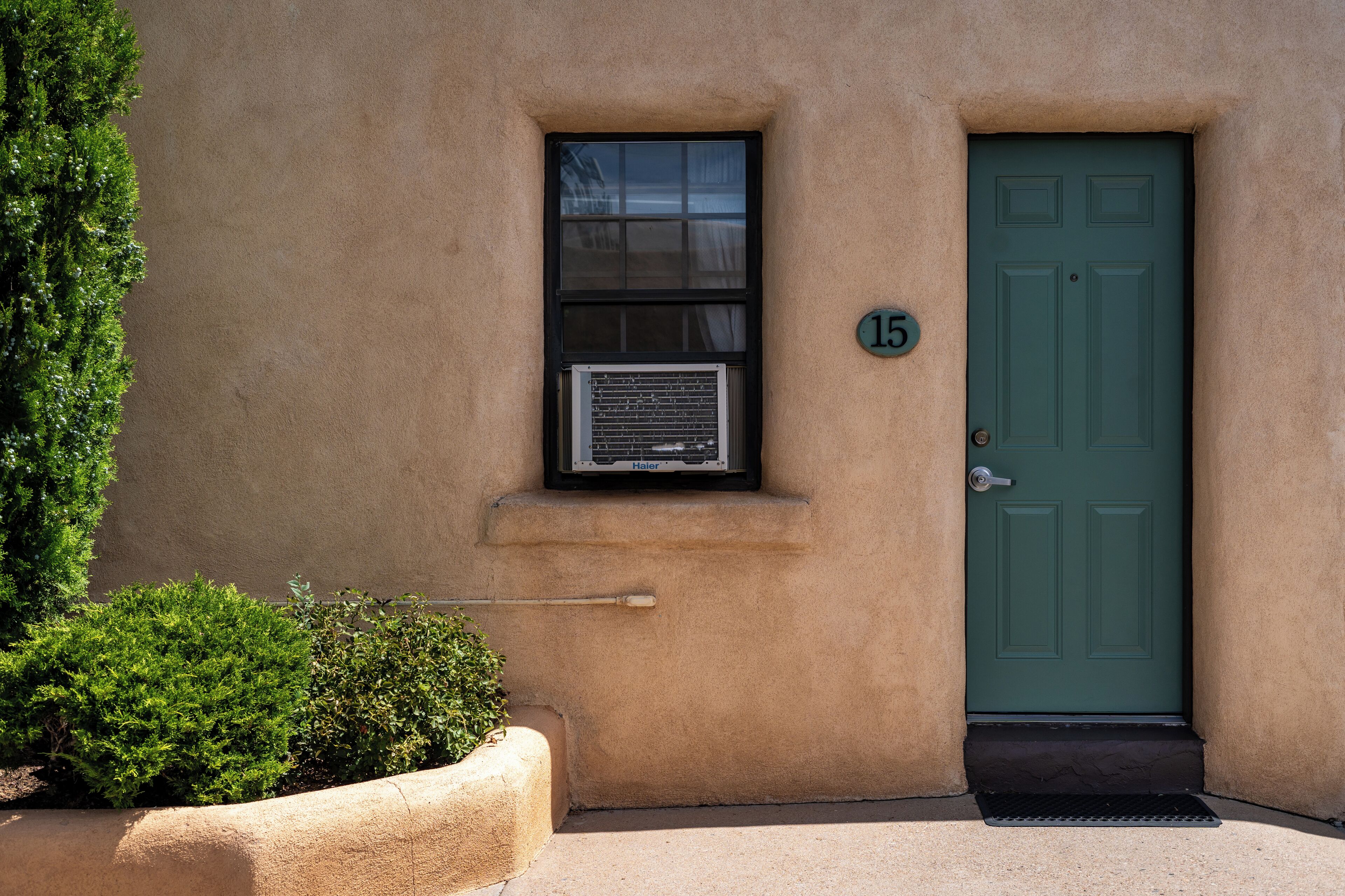 Un bâtiment avec une porte verte, une fenêtre équipée d’un climatiseur et un petit panneau indiquant le numéro « 15 ».