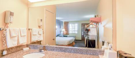 A hotel bathroom with a granite countertop, a sink, a hairdryer, a mirror, and a coffee maker.