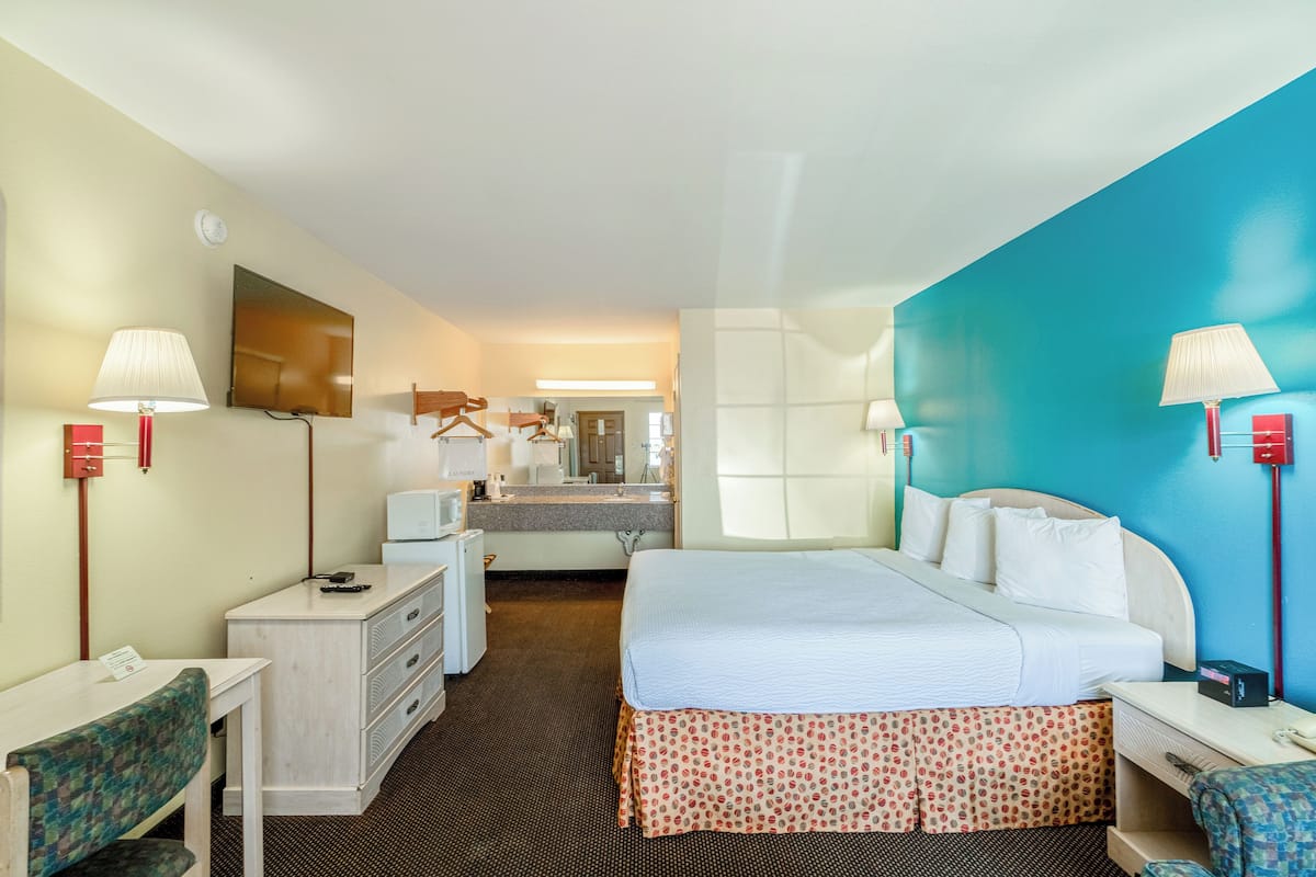 A hotel room with a bed, desk, chair, and a bathroom with a mirror and sink.