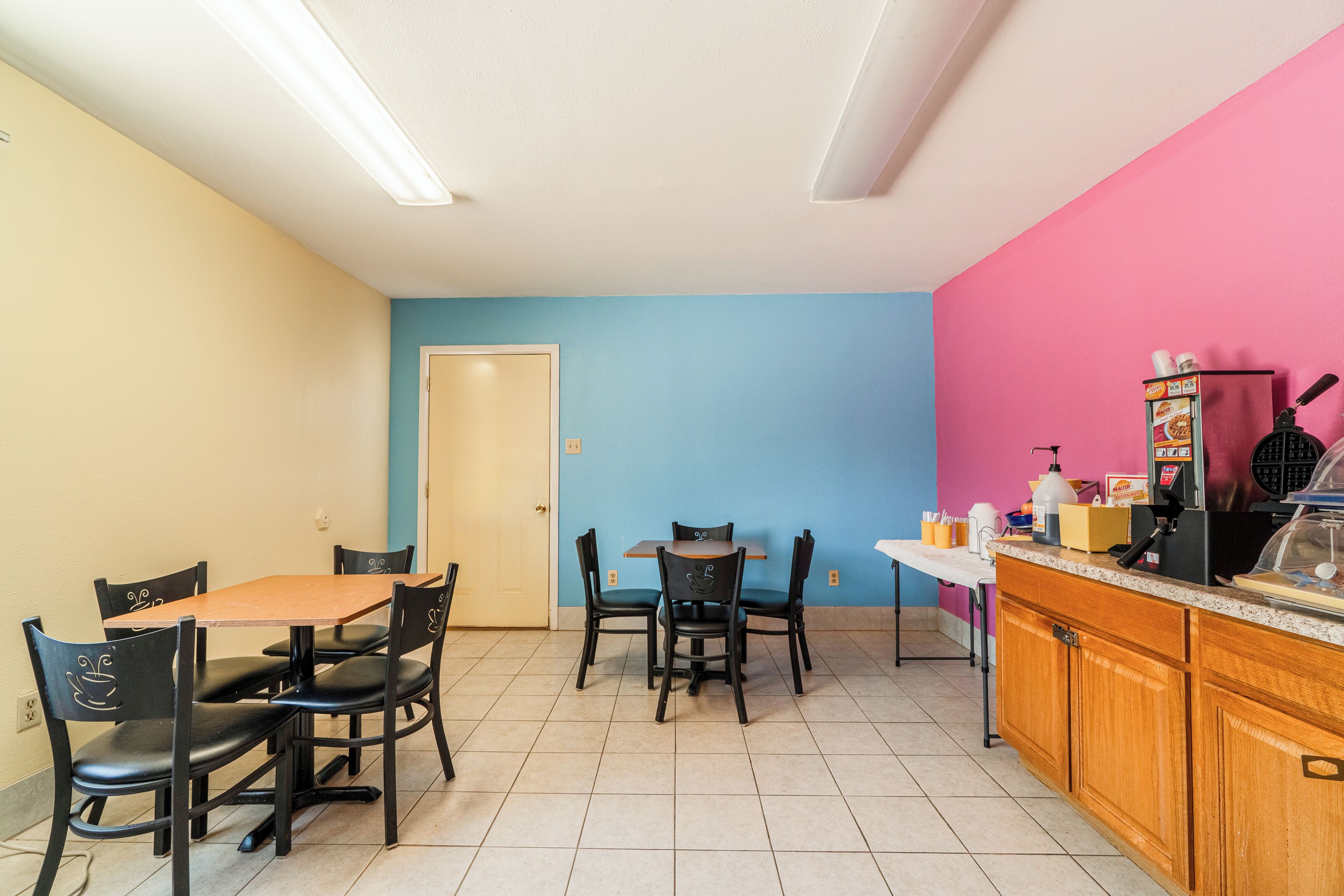 A dining area with a wooden table and chairs, a kitchen counter with appliances, and a door leading to another room.