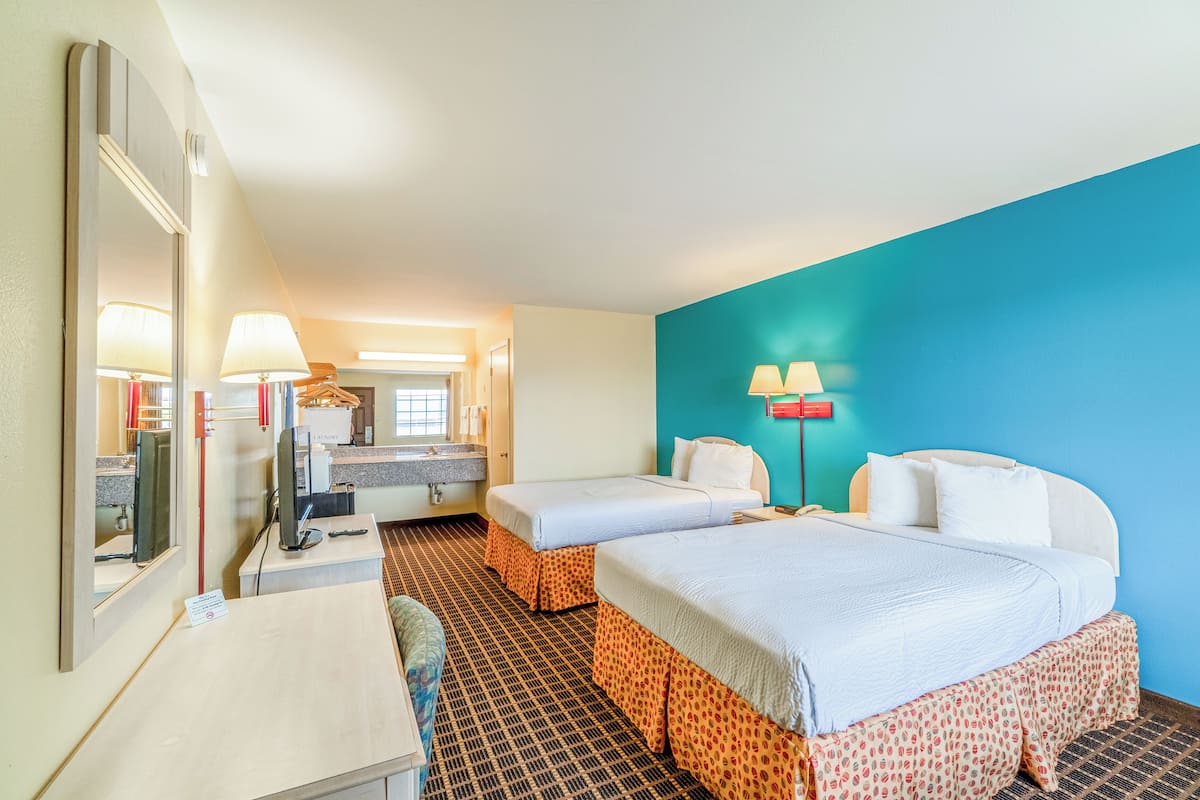 A hotel room with two beds, a desk, a mirror, a bathroom, and a blue accent wall.