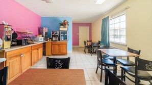 A kitchen with wooden cabinets, a microwave, and a coffee machine. There is a dining area with a table and chairs. The walls are painted in different colors. - Shale Inn Andrews (Andrews)
