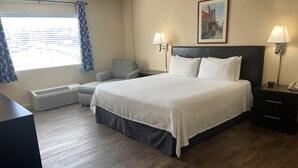 A hotel room with a large bed, two bedside lamps, a chair, a desk, a heater, and a window with curtains. - University Inn Durham next to Duke University Medical Center (Durham)