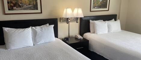 Ett hotellrum med två sängar, ett nattduksbord med en lampa och två inramade tavlor på väggen.