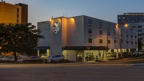 A modern hotel with a prominent logo on the facade, a covered entrance, and a parking lot with several cars. - University Inn Durham next to Duke University Medical Center (Durham)