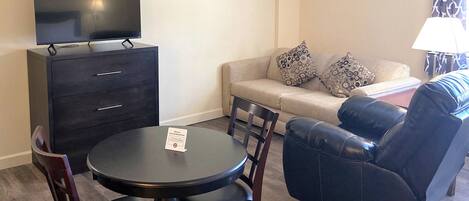 A living room with a TV, a sofa, a coffee table, and a dining table with chairs.