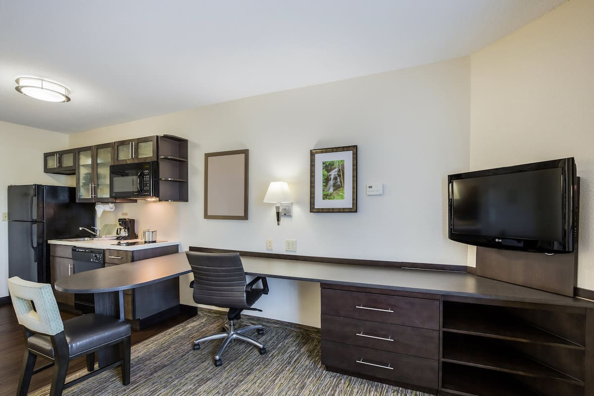 Habitación de hotel compacta con kitchenette, televisión de pantalla plana, escritorio y silla.