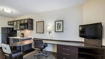 Quarto de hotel compacto com cozinha compacta, televisão de tela plana, escrivaninha e uma cadeira.