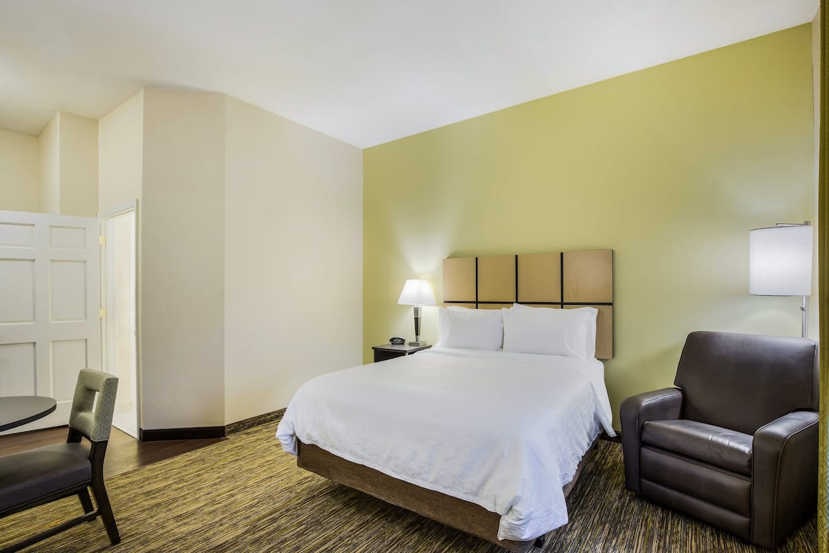 Una habitación de hotel con una cama, una silla, un escritorio y una lámpara.