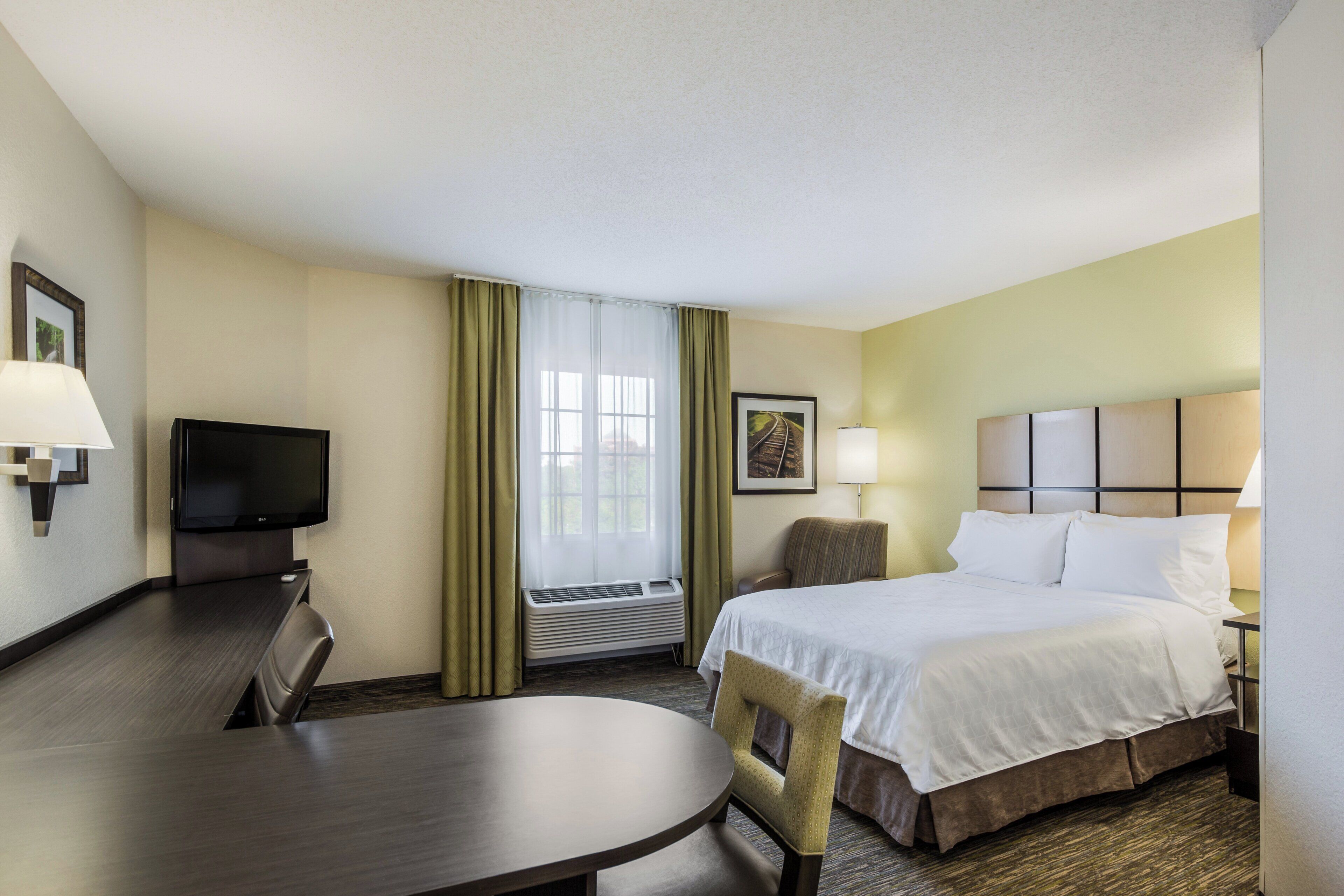 A hotel room with a bed, a desk, a chair, a television, and a window with curtains.