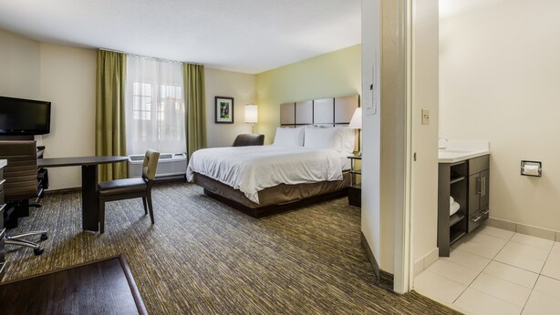 A hotel room with a bed, a desk, a chair, a television, and a bathroom with a sink and mirror. - Candlewood Suites Virginia Beach Town Center by IHG (Virginia Beach)