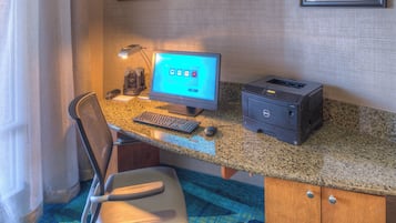 Habitación de hotel con escritorio, computadora, impresora y una silla.