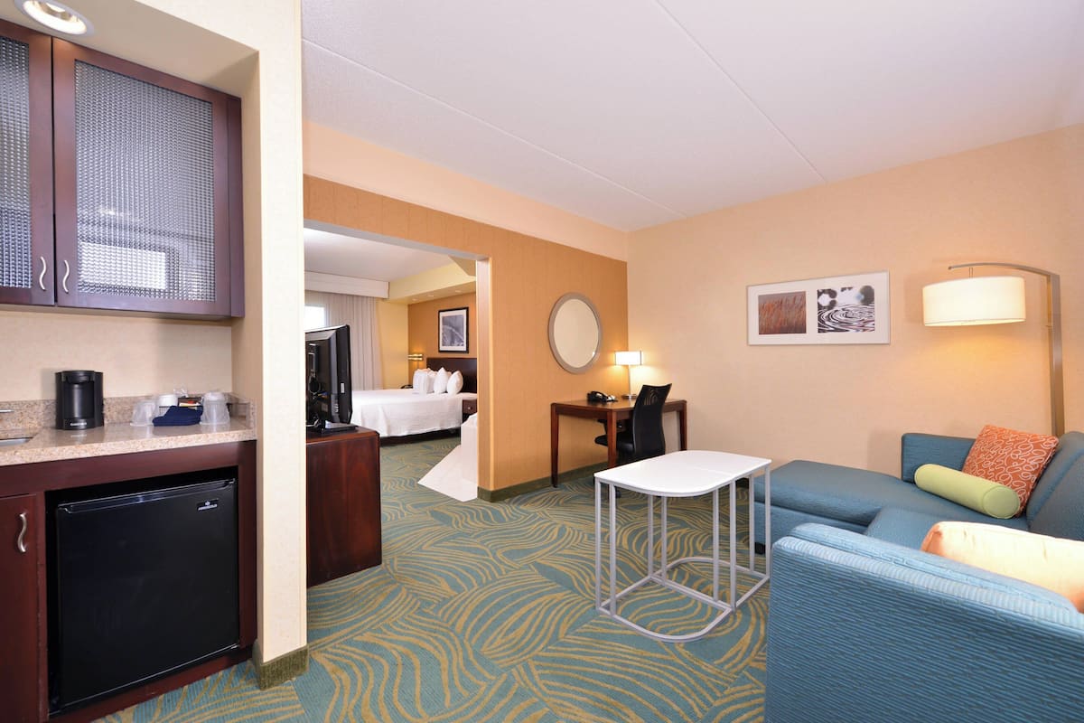 A hotel room with a kitchenette, a bed, a desk with a chair, a sofa, and a small table.